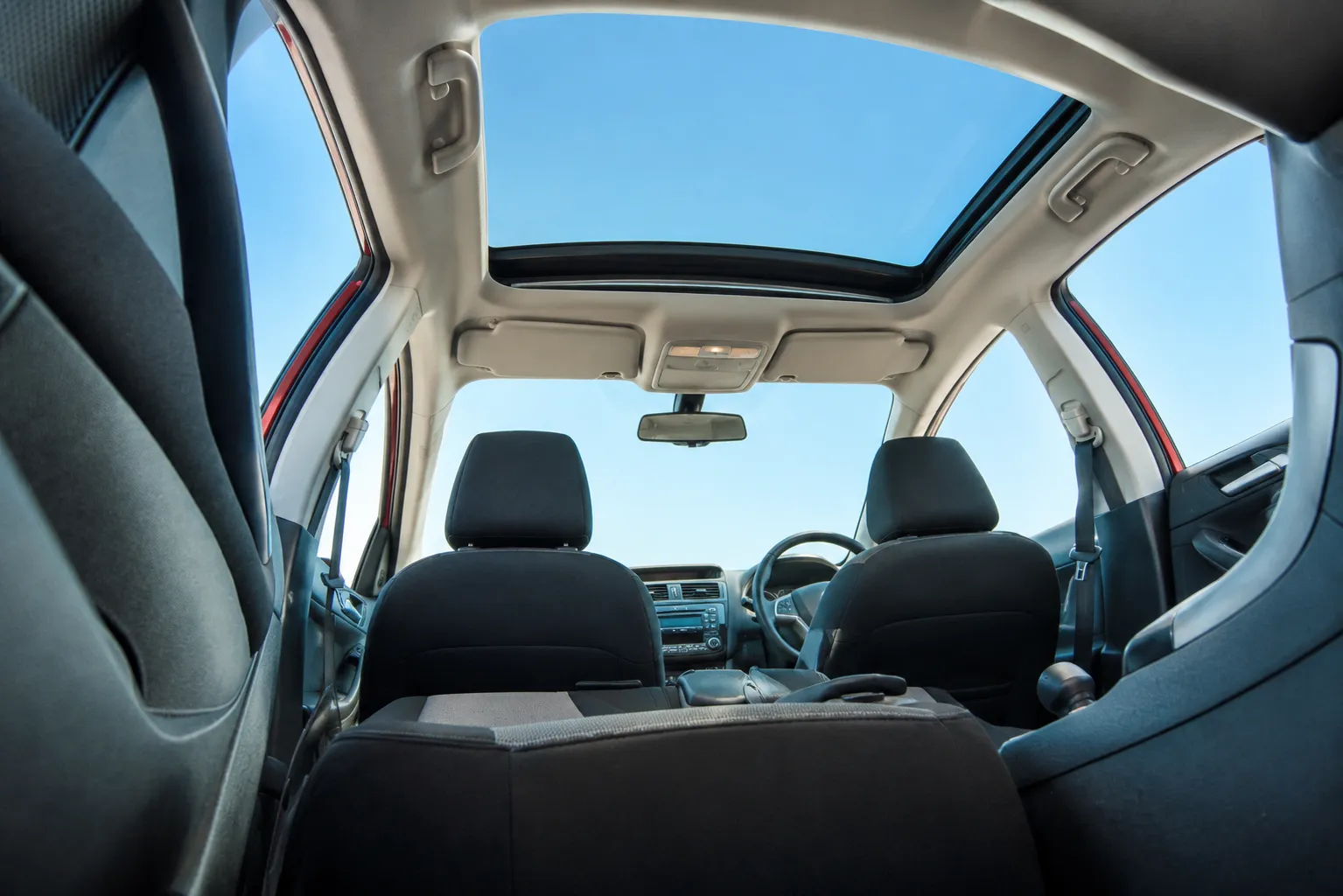 View from inside a vehicle cabin looking up through an intact panoramic moonroof against a clear blue sky.